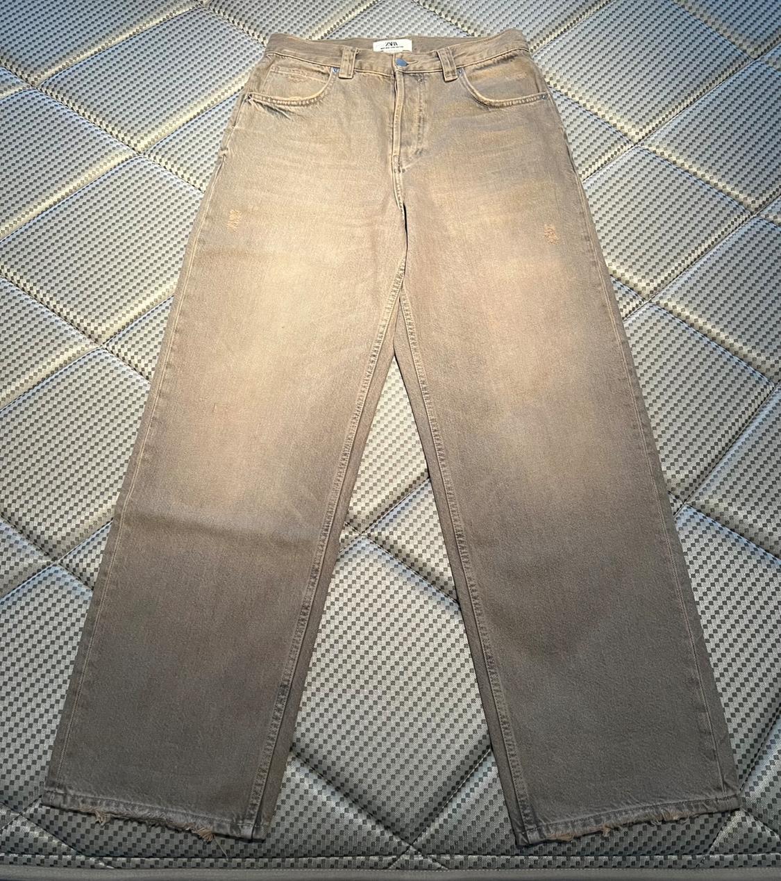 Grey straight-cut jeans on a grey padded surface with a checked pattern. Visible label on the waistband.