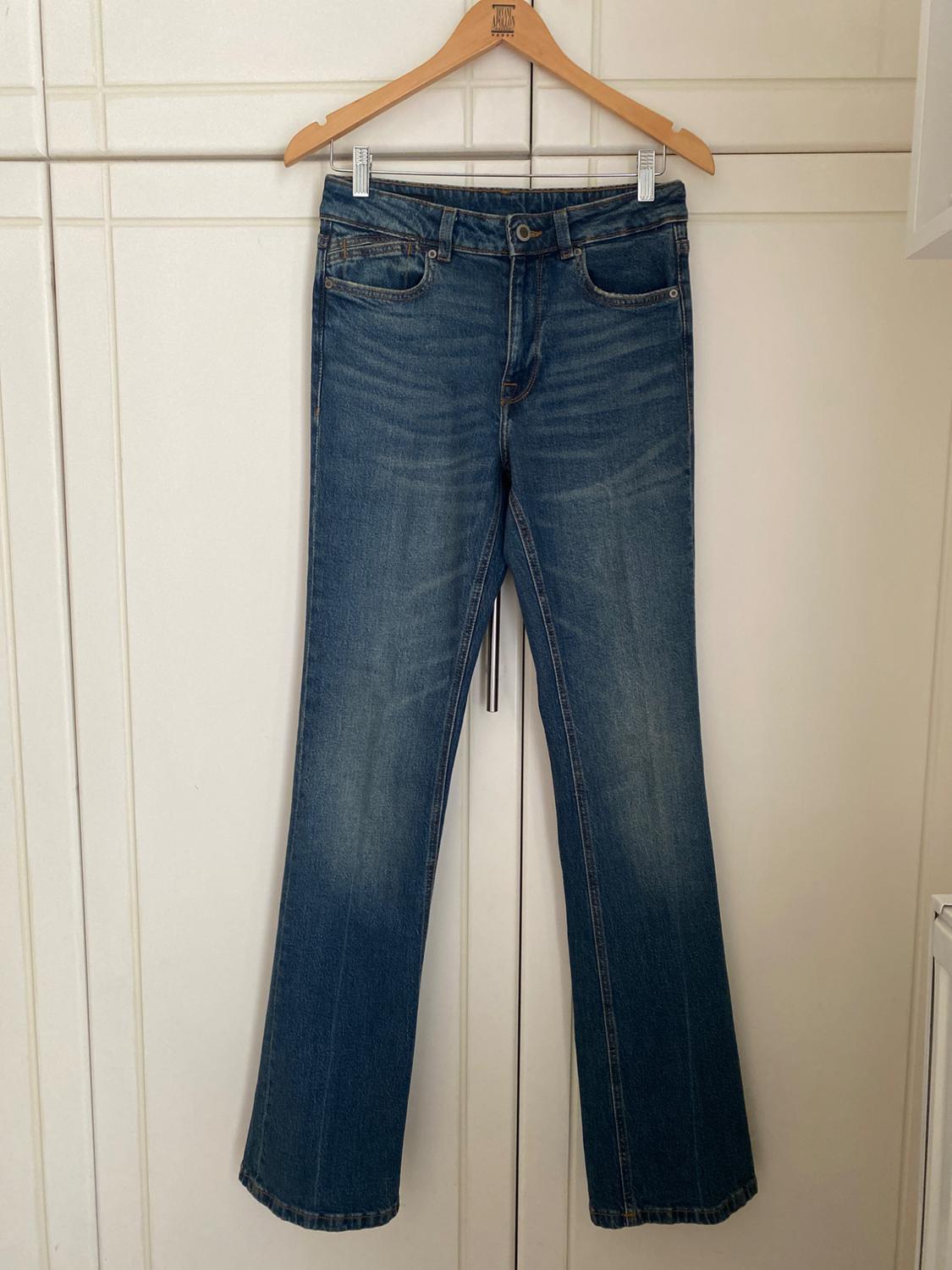Straight-leg blue jeans hanging on a wooden hanger over a white door.