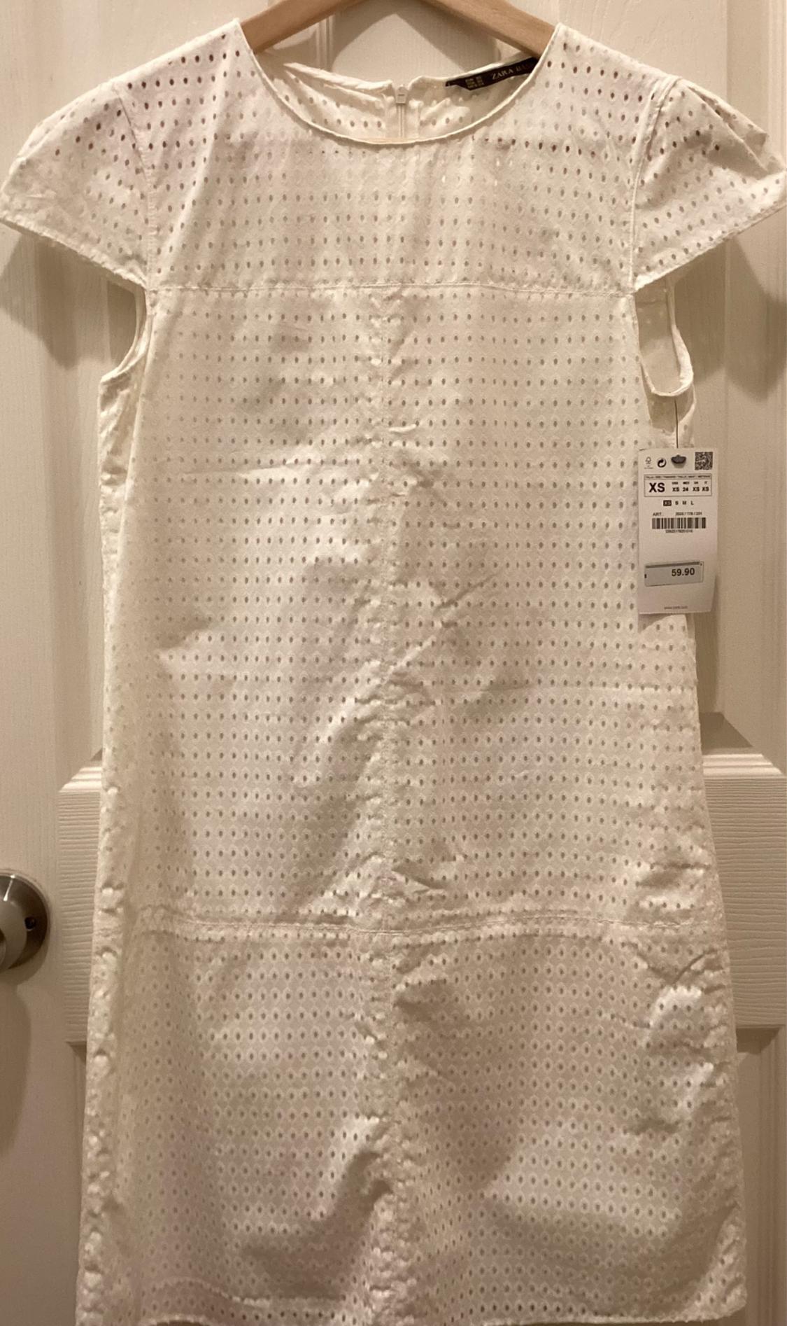 Front view of a white dress with perforations and short sleeves, hanging on a hanger.