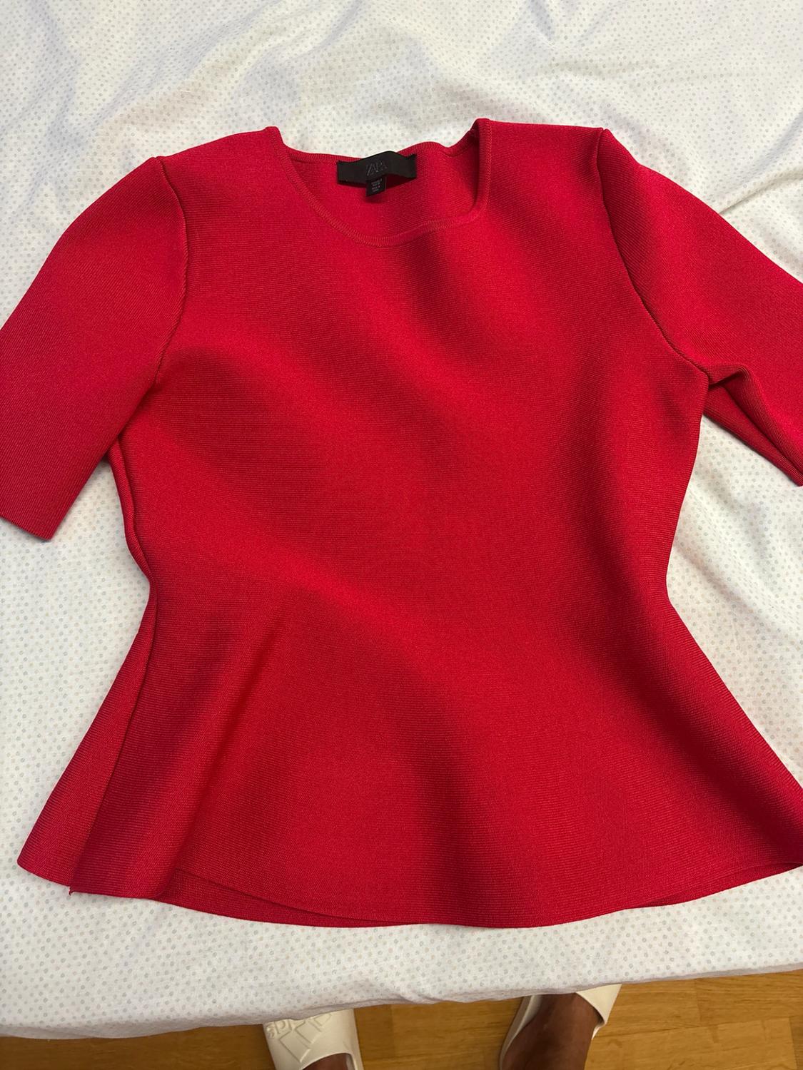 Red short-sleeved top with a flared hem over white fabric with spots. At the bottom, feet wearing white shoes are visible.