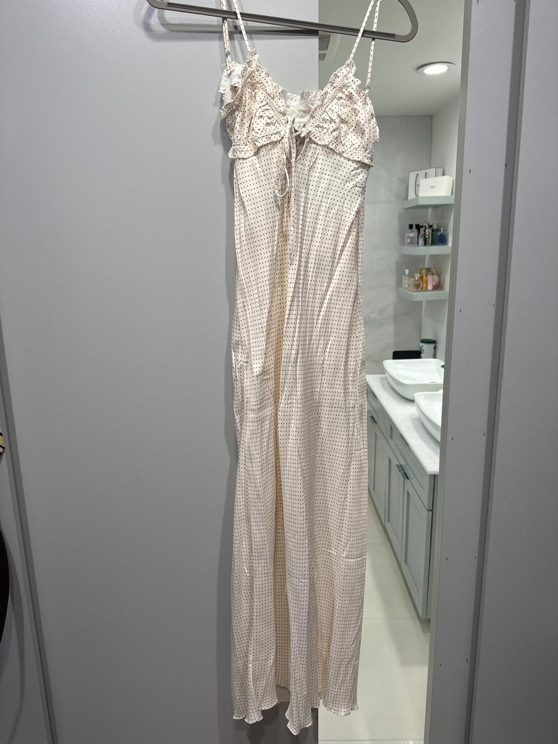 Long spaghetti-strap dress with small polka dot print, hanging on a hanger in a modern bathroom.