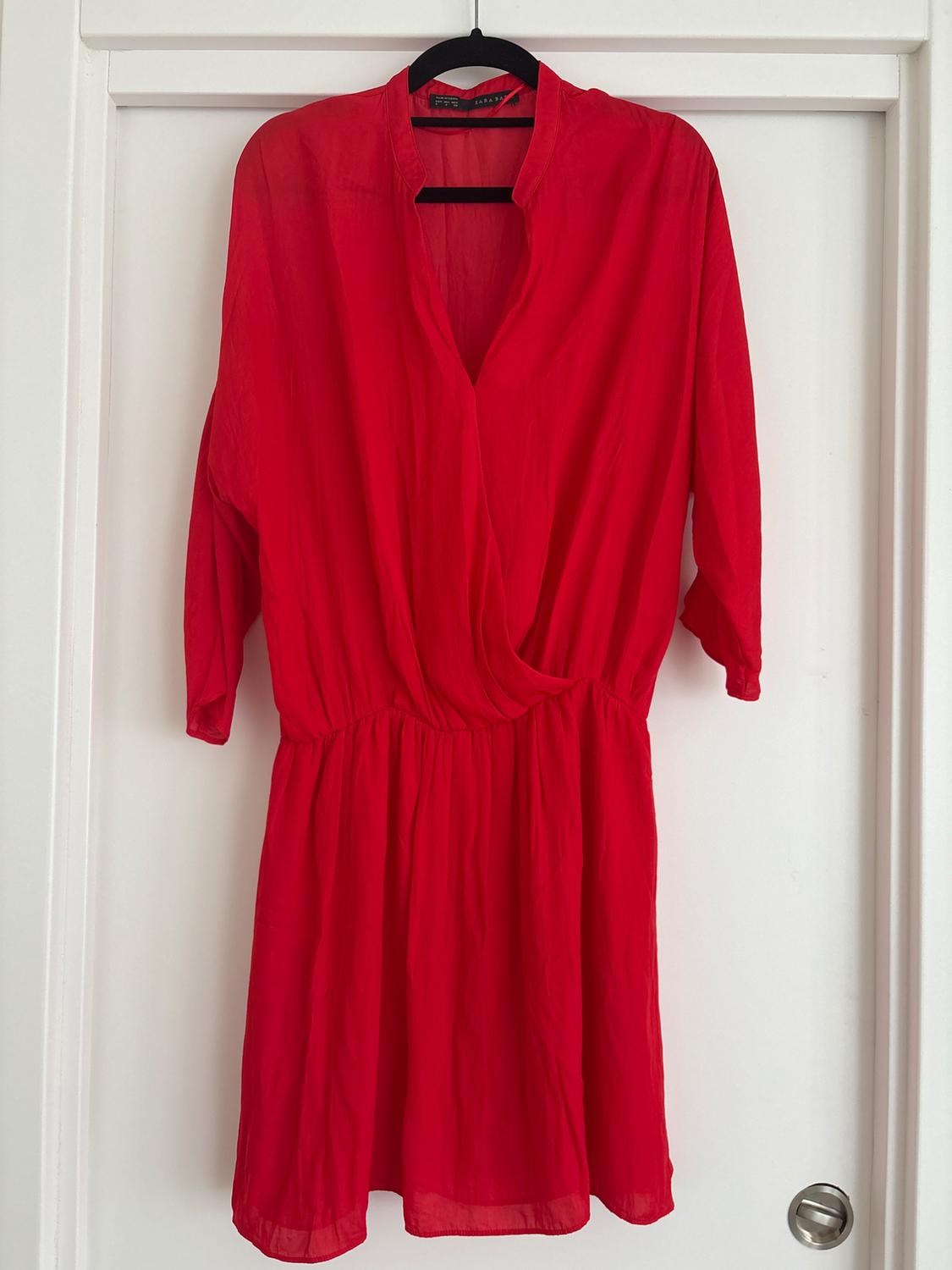 Long-sleeved red dress hanging on a black hanger over a white door. Lightweight fabric with a V-neckline and elasticated waist.