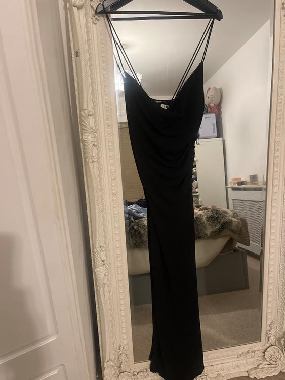 Black slip dress hanging on an ornate white-framed mirror. Reflection of a room with a bed and decorations.