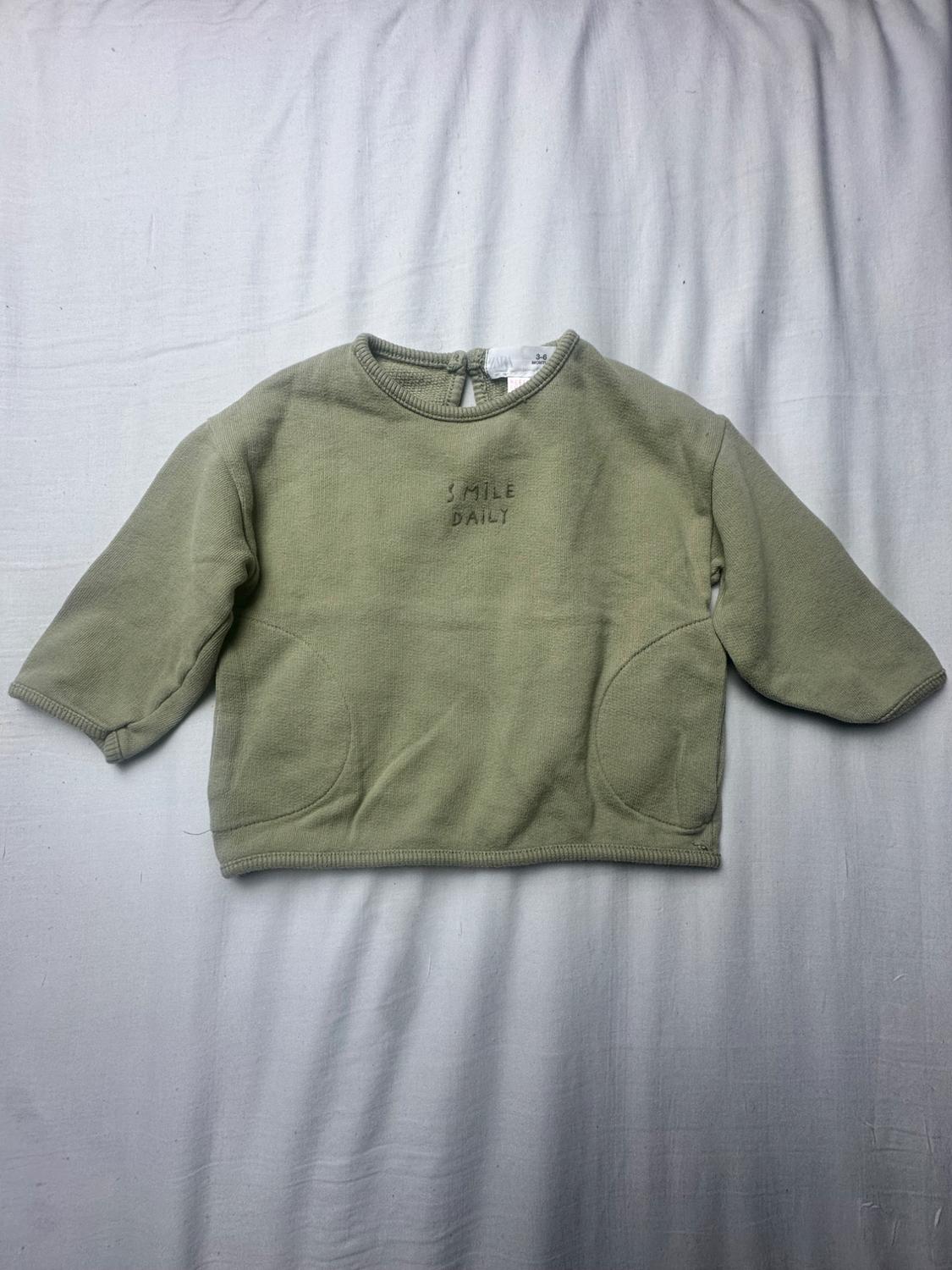 Olive green baby hoodie with a crew neck, long sleeves, and two pockets. Features embroidered text "SMILE DAILY" on the chest.