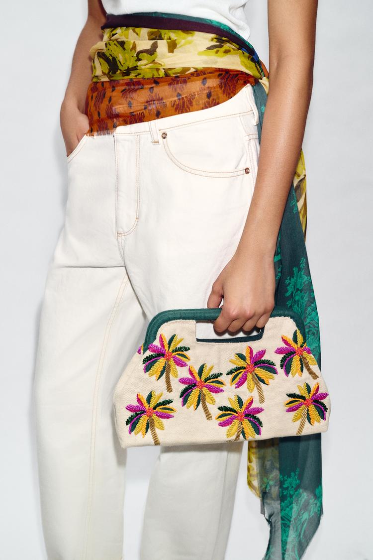 Detailní záběr na vícebarevnou pouch kabelku s květinovou výšivkou, pevným držadlem a magnetickým zapínáním. Vnitřní kapsa na zip.