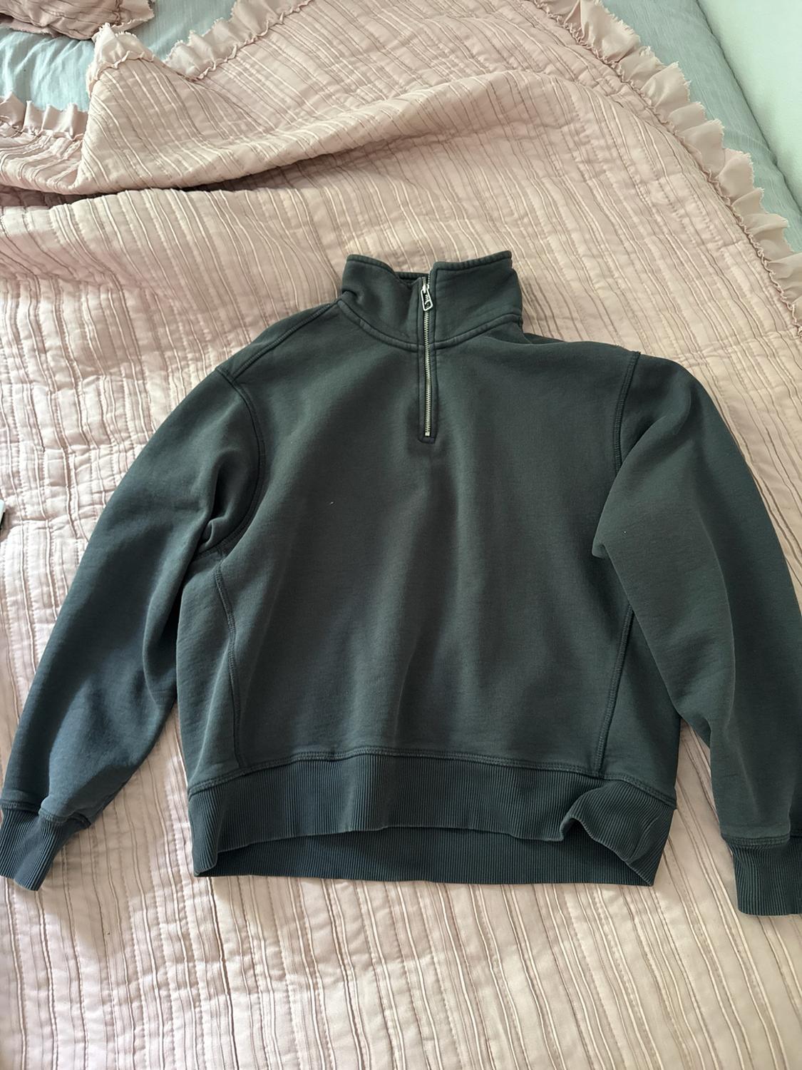 Dark gray half-zip sweatshirt over a pink ruffled bedspread, conveying a casual and homey style.