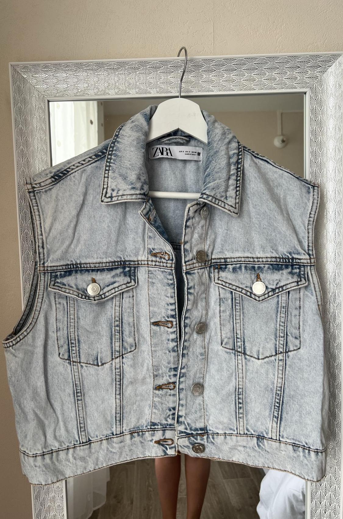 Front view of light blue denim waistcoat with front flap pockets and metallic buttons.
