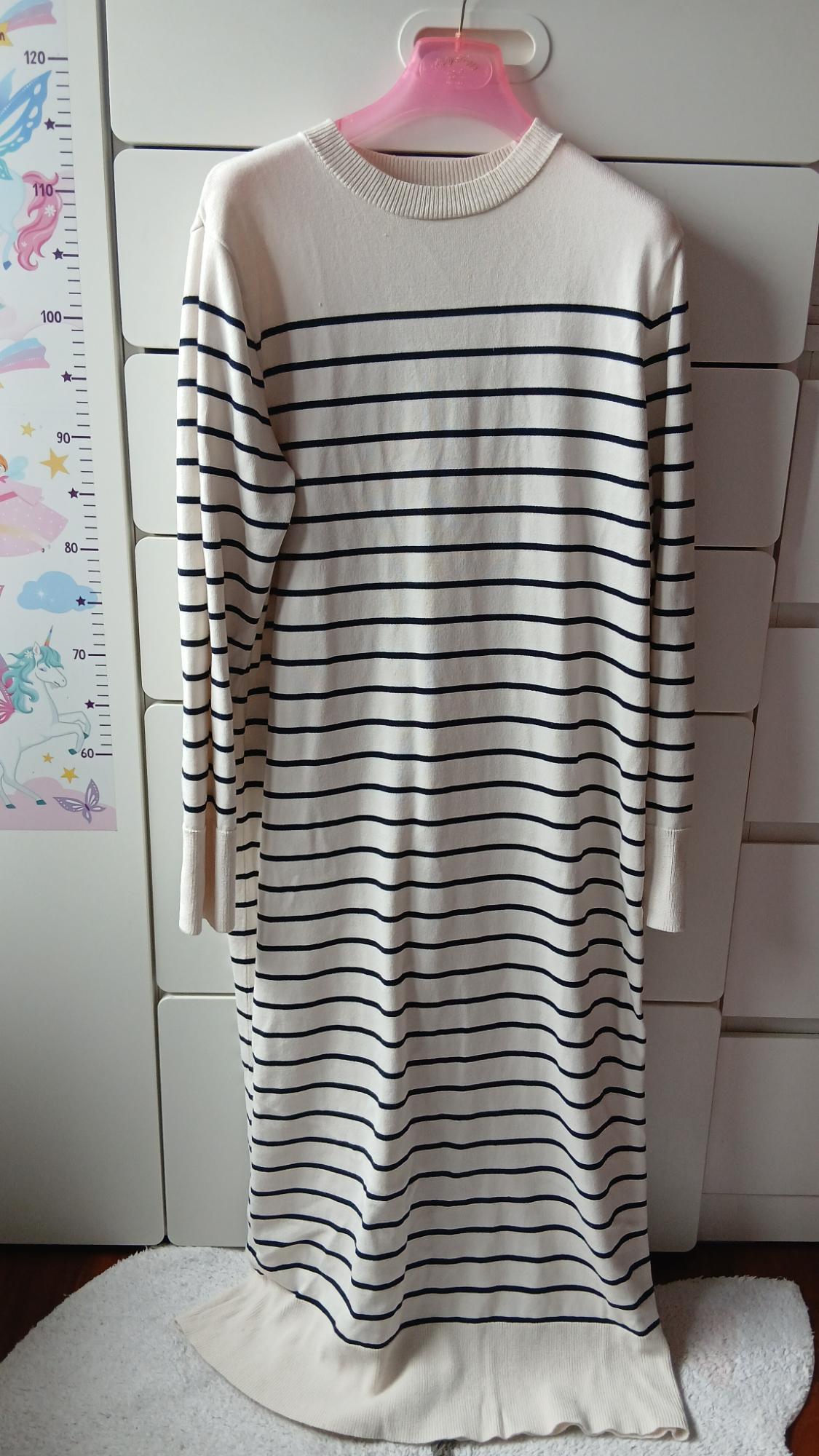 Long dress with horizontal black stripes on a white background, hanging on a pink hanger in front of a white cabinet.