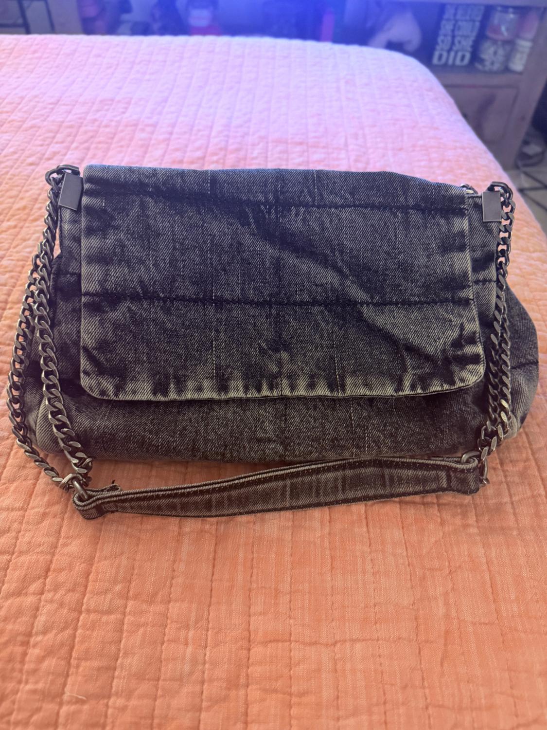 Dark gray denim bag with a flap and chain on an orange bedspread. In the background, it reads: SHE BELIEVED SHE COULD SO SHE DID.