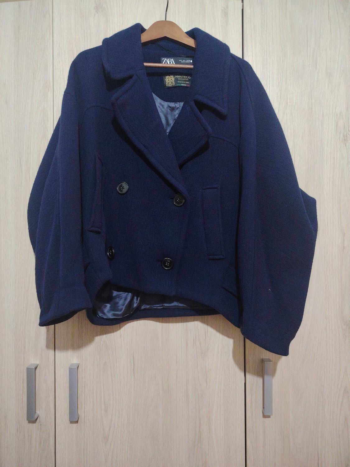 Dark blue double-breasted coat hanging on a wooden hanger in front of a light wood wardrobe.