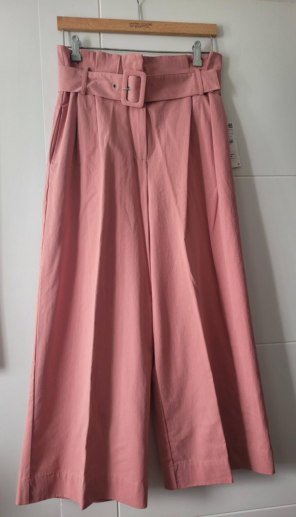 Pink culotte trousers with a wide belt and buckle, hanging on a wooden hanger from United Colors of Benetton.