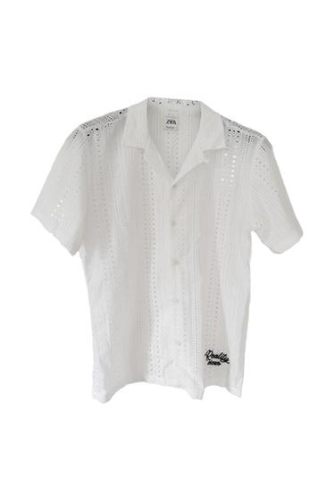 White short-sleeved shirt with a perforated design. Includes a Zara label and the text "Reality views" embroidered at the bottom.