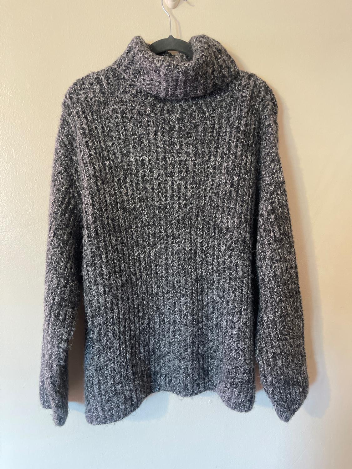 Chunky gray knit sweater with a high collar, hanging on a hanger against a beige wall.