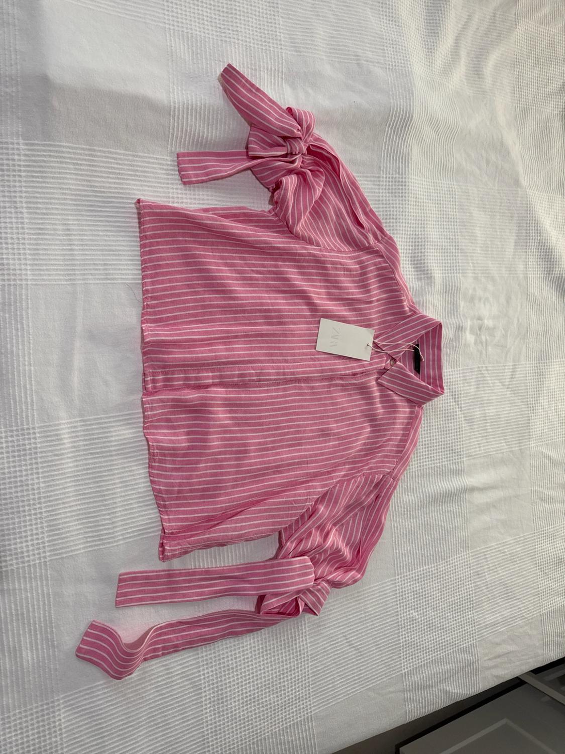 Pink and white striped shirt with bows on the sleeves and a ZARA label, on a textured white surface.