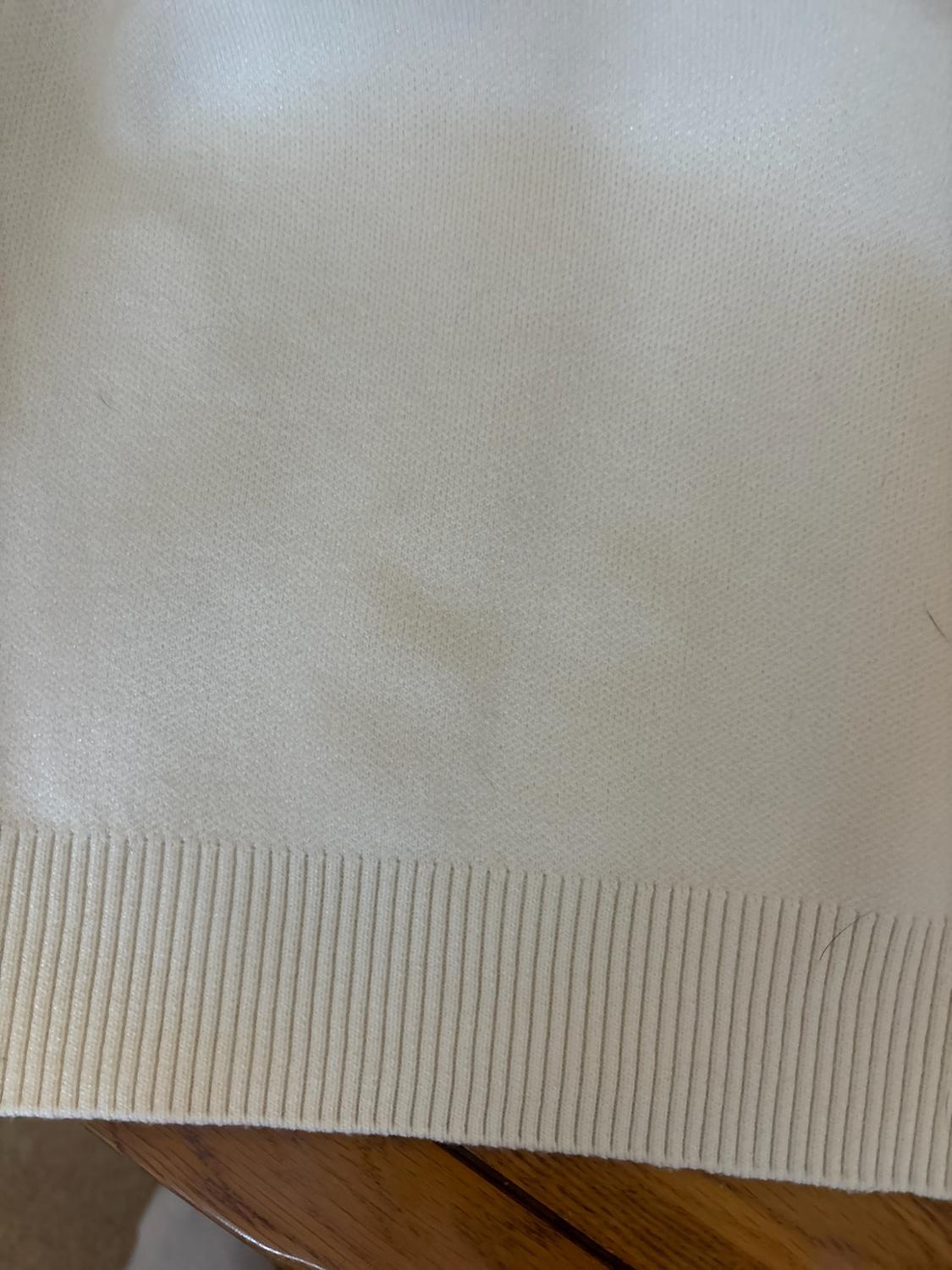 Close-up of a cream knitted garment with a ribbed hem on a wooden surface.