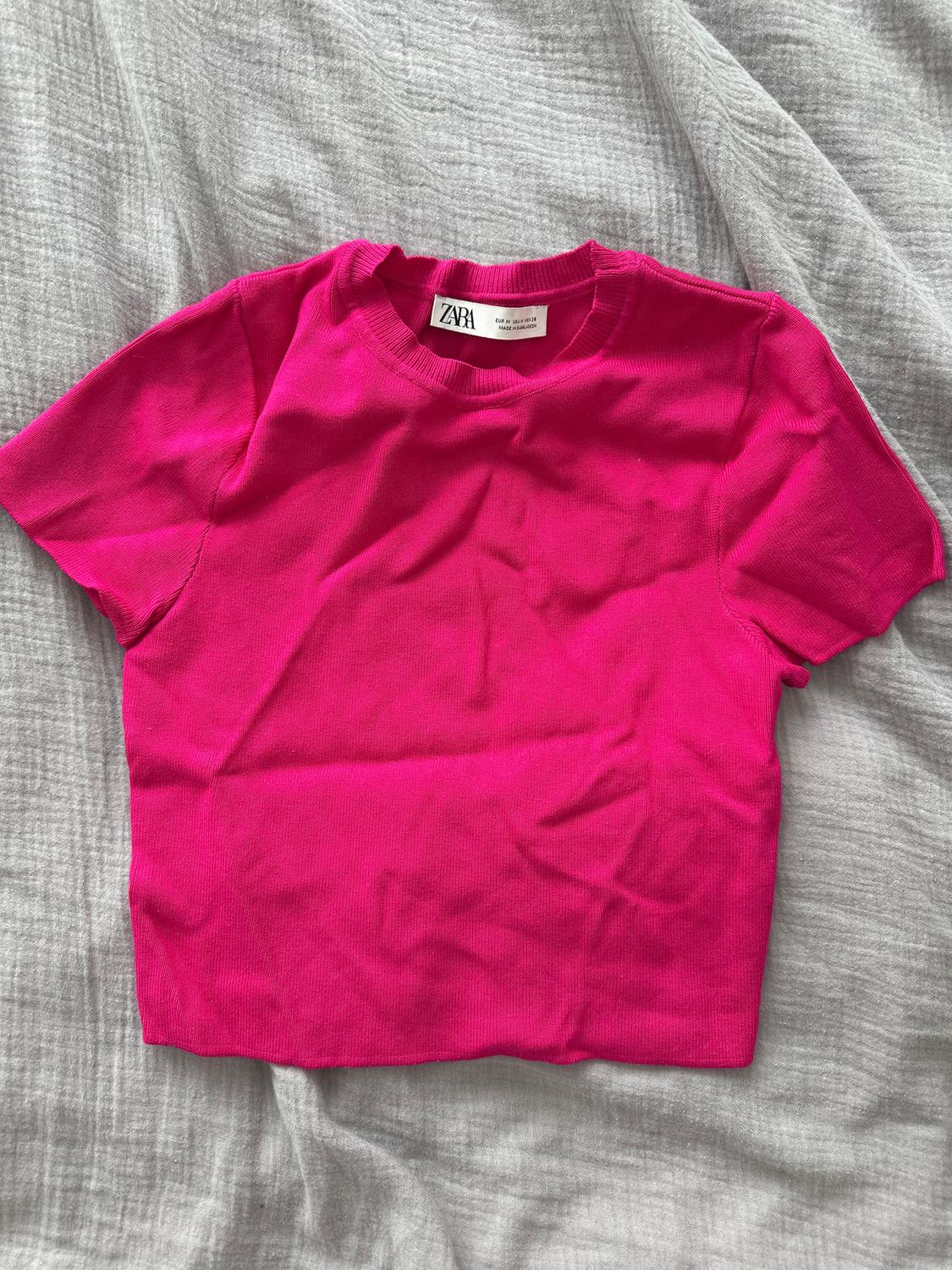 Fuchsia pink short-sleeved t-shirt on grey fabric. Visible label with text: "ZARA".