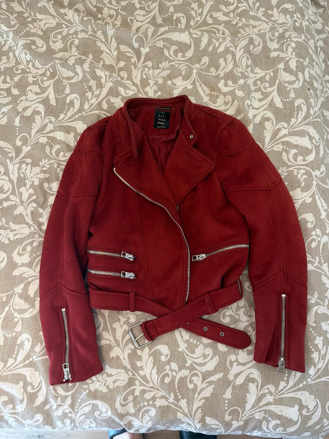 Red biker jacket with asymmetrical zips and belt, on a floral-patterned bedspread. Text: trf outer wear.