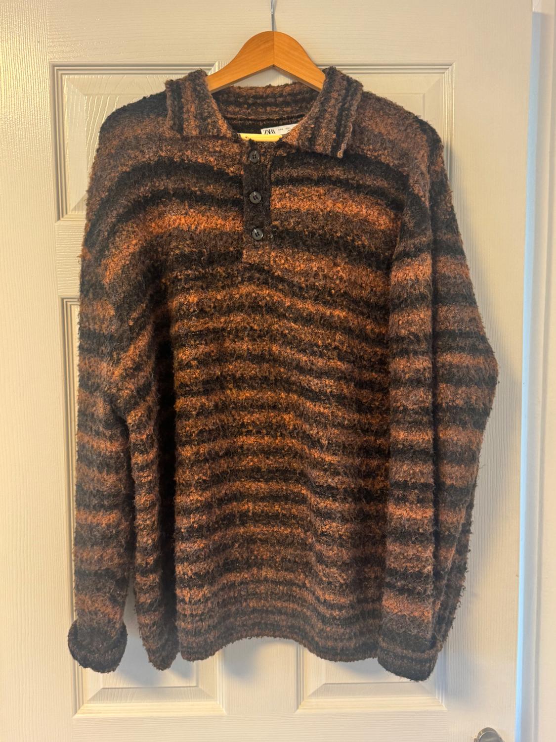 Brown and black striped jumper with a collar and buttons, hanging on a wooden hanger over a white door.