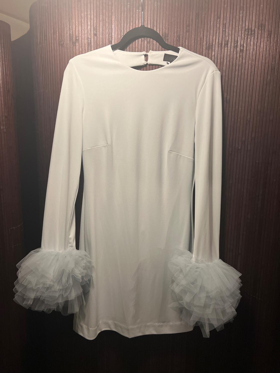 Long-sleeved white dress with voluminous tulle cuffs, hanging on a black hanger against a brown wooden background.