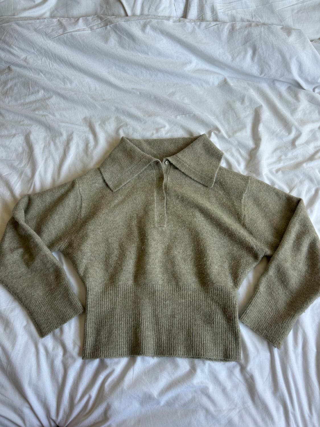 Grey woollen polo-neck jumper with buttons, laid out on a bed with crumpled white sheets.