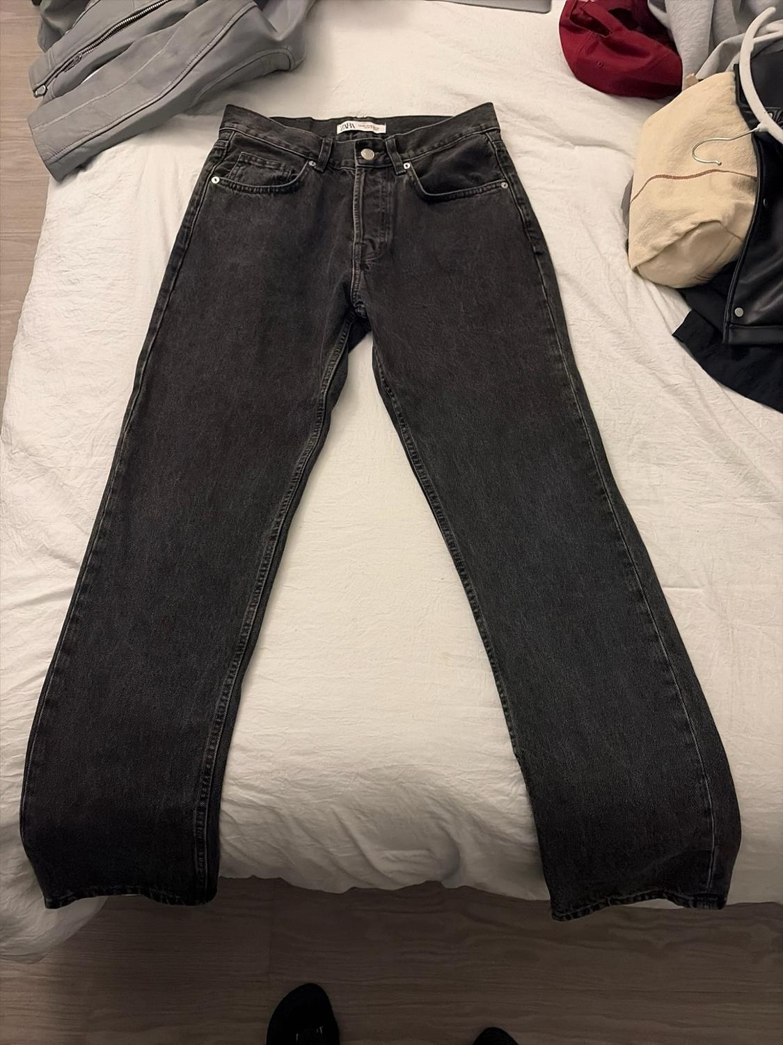 Black jeans laid out on a white bed next to other clothing. ZARA is visible on the label.