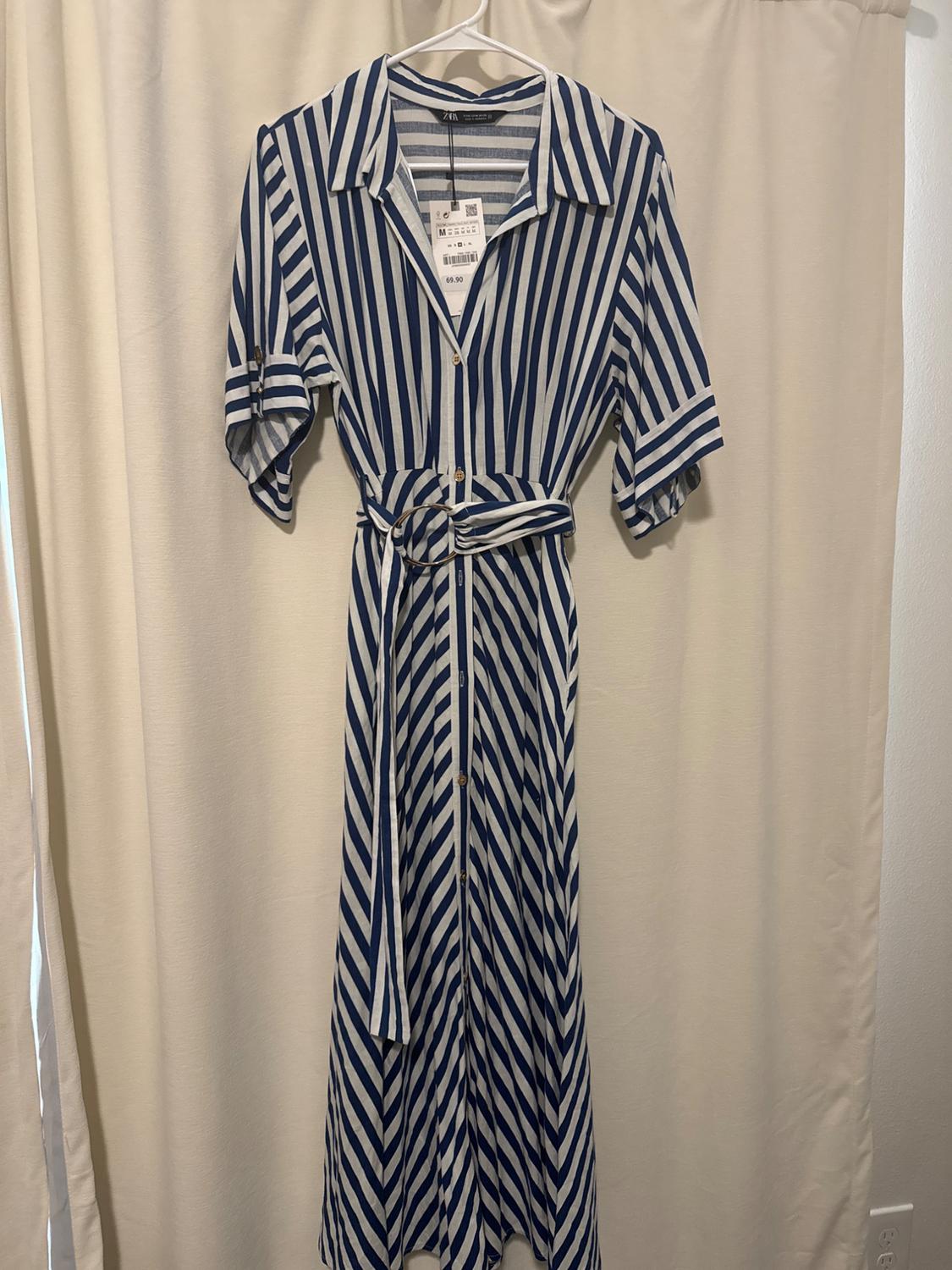 Blue and white striped dress hanging on a hanger over a beige curtain. It has a price tag of 69.90.
