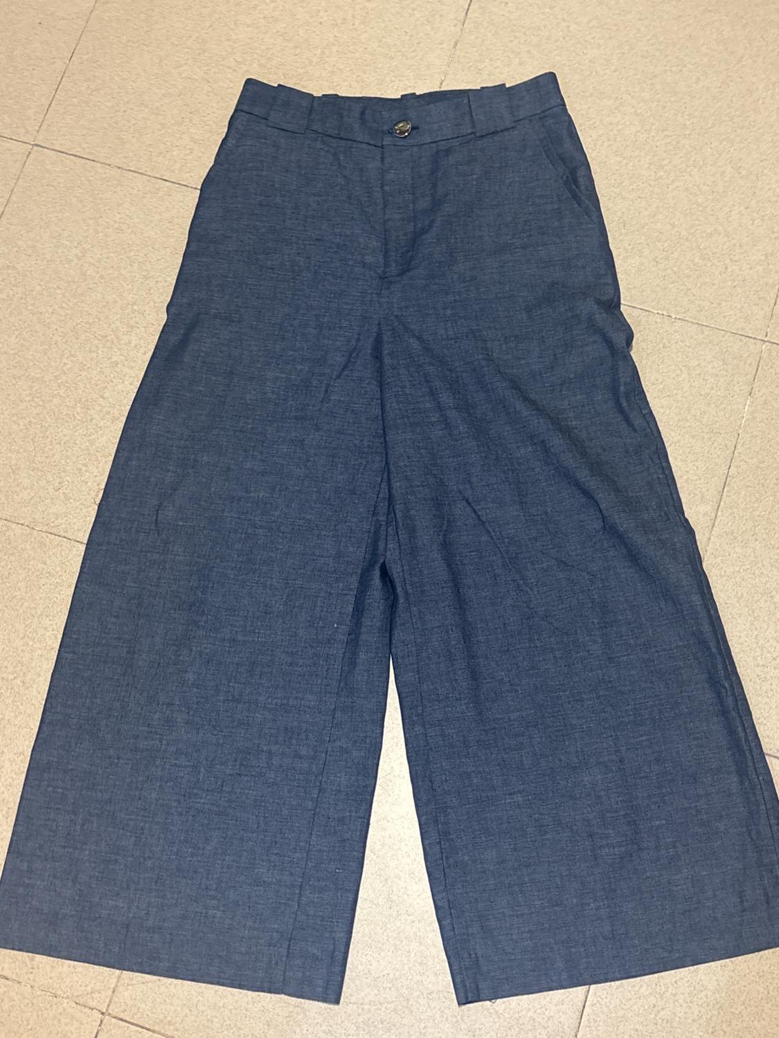Dark blue wide-leg fabric trousers with a button and zip, placed on a beige tiled floor.