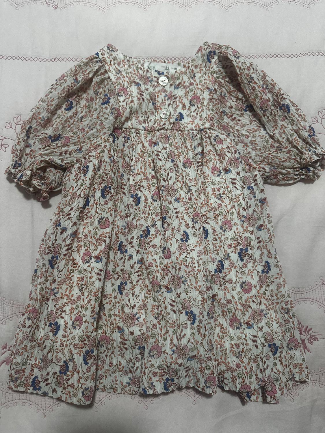 Children's dress with a floral print in pink and blue tones, with puff sleeves and front buttons, on a light background with embroidery.