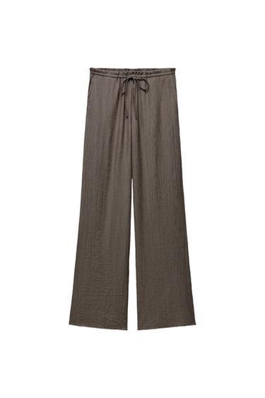 Brown wide-leg trousers with a crinkled texture and an adjustable drawstring elasticated waist, on a white background.