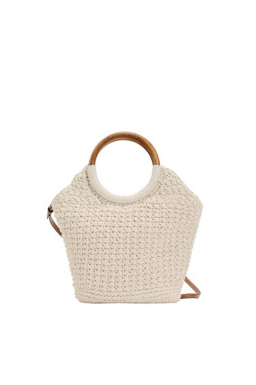 Cream-colored woven bag with circular wooden handles and a thin brown strap on a white background.