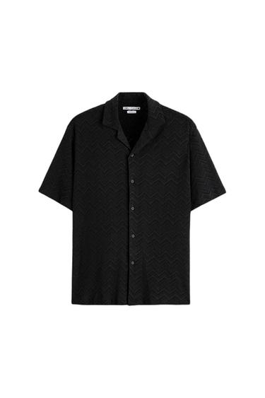 Black short-sleeved shirt with a zigzag pattern. Open collar and front buttons. Visible label on the inside of the collar.