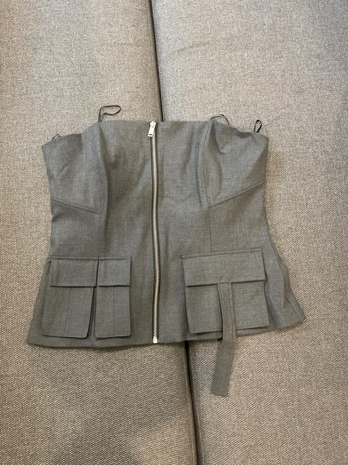 Grey waistcoat with front zip and large pockets, on a grey sofa.