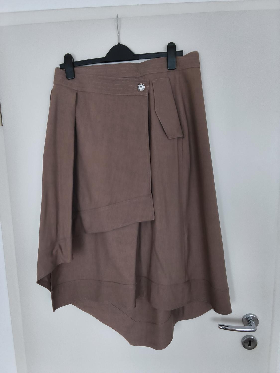 Brown asymmetrical skirt hanging on a black hanger over a white door, with button detail and decorative belt.