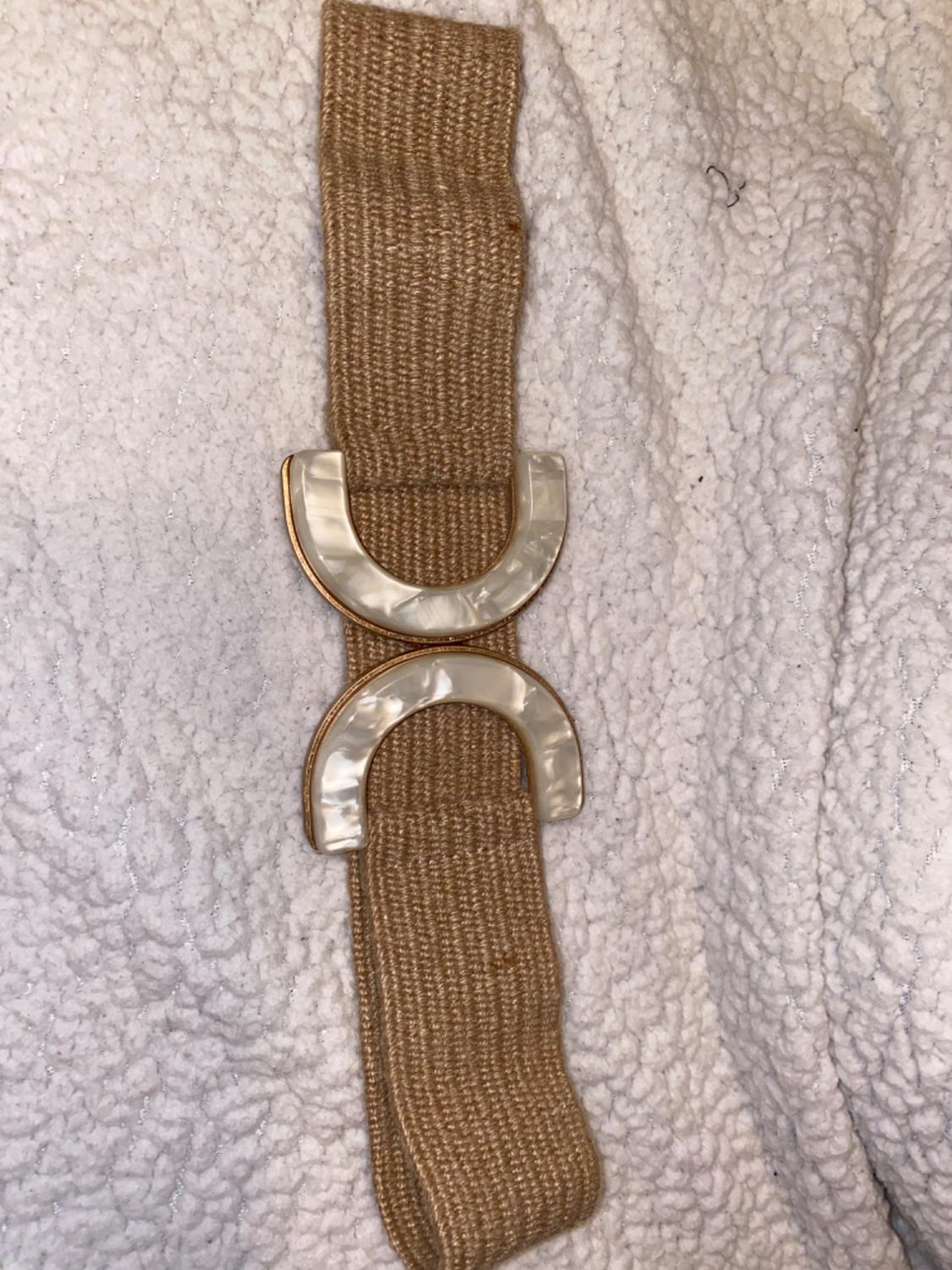 Brown woven belt with a mother-of-pearl half-moon buckle on a textured white fabric background.