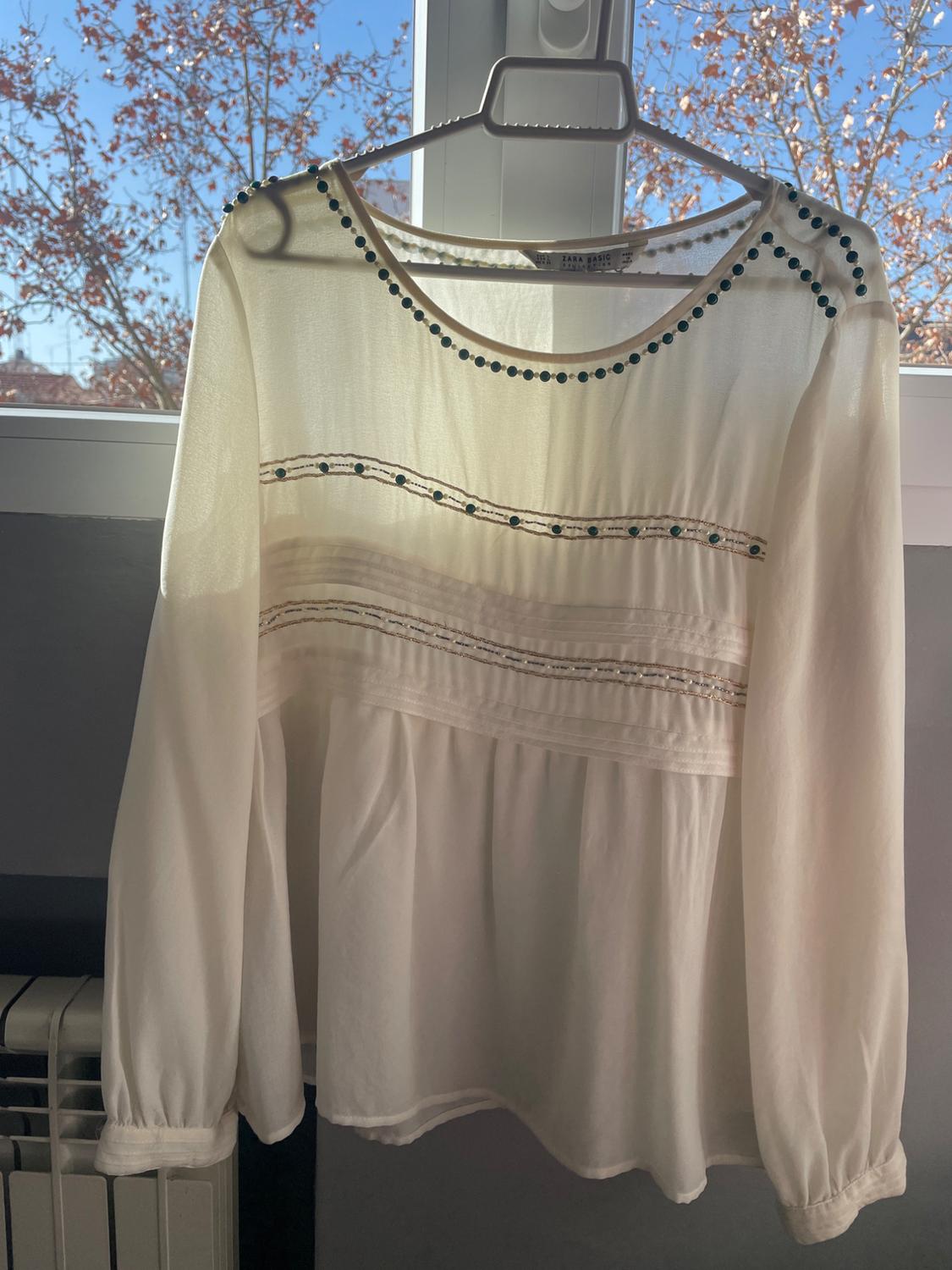 Front view of a white blouse with stud details on the collar and horizontal decorative lines.