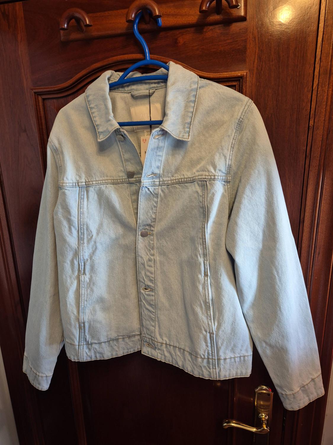 Light blue denim jacket hanging on a blue hanger on a dark wooden door.