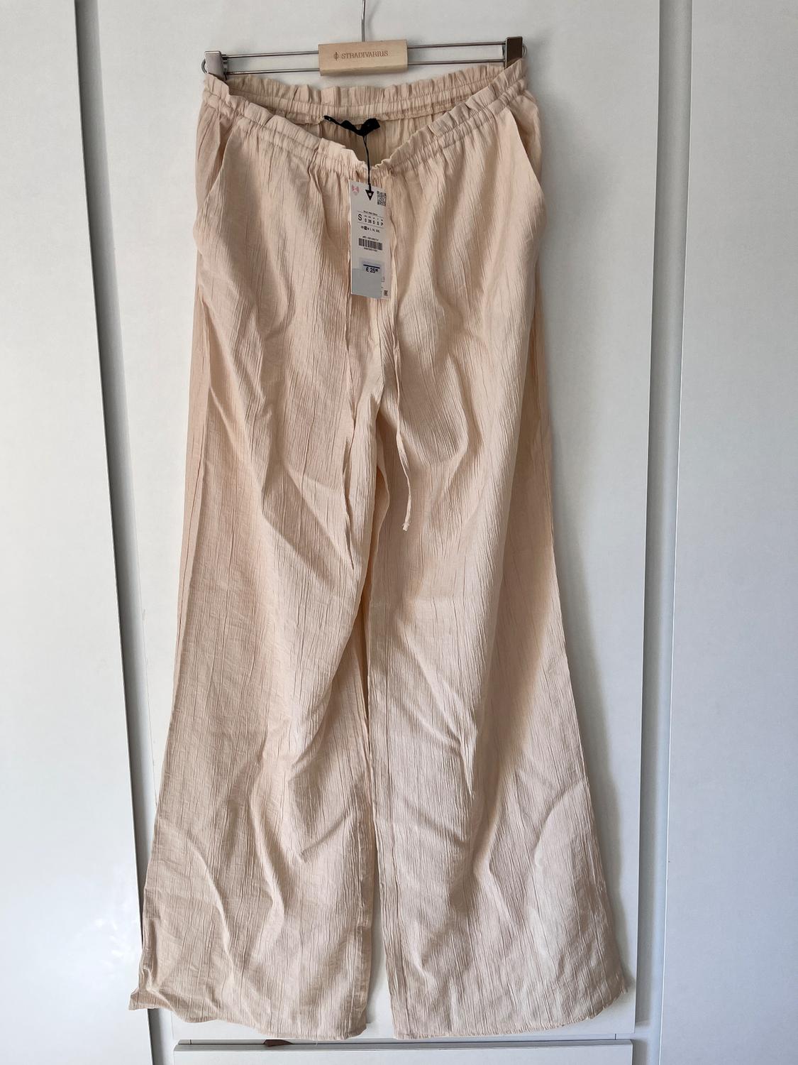 Light beige fabric trousers hanging on a Stradivarius hanger, with a visible tag showing size and price.