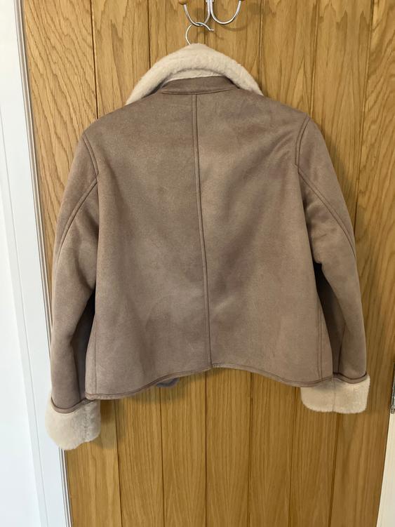 Beige jacket with a white plush lining on the collar and cuffs, hanging on a light wooden door.