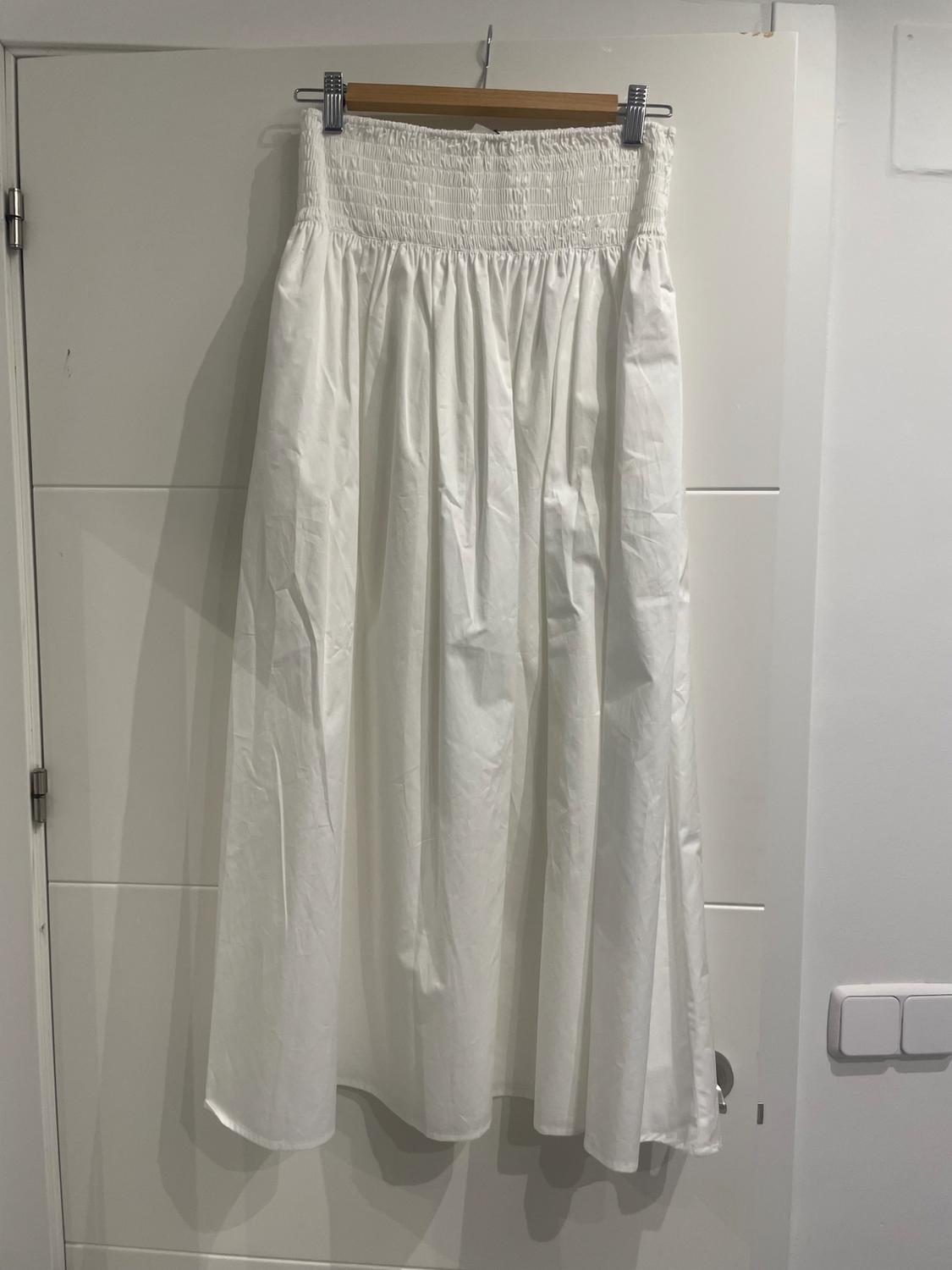 Long white skirt with shirred elastic waistband, hanging on a wooden hanger over a white door.