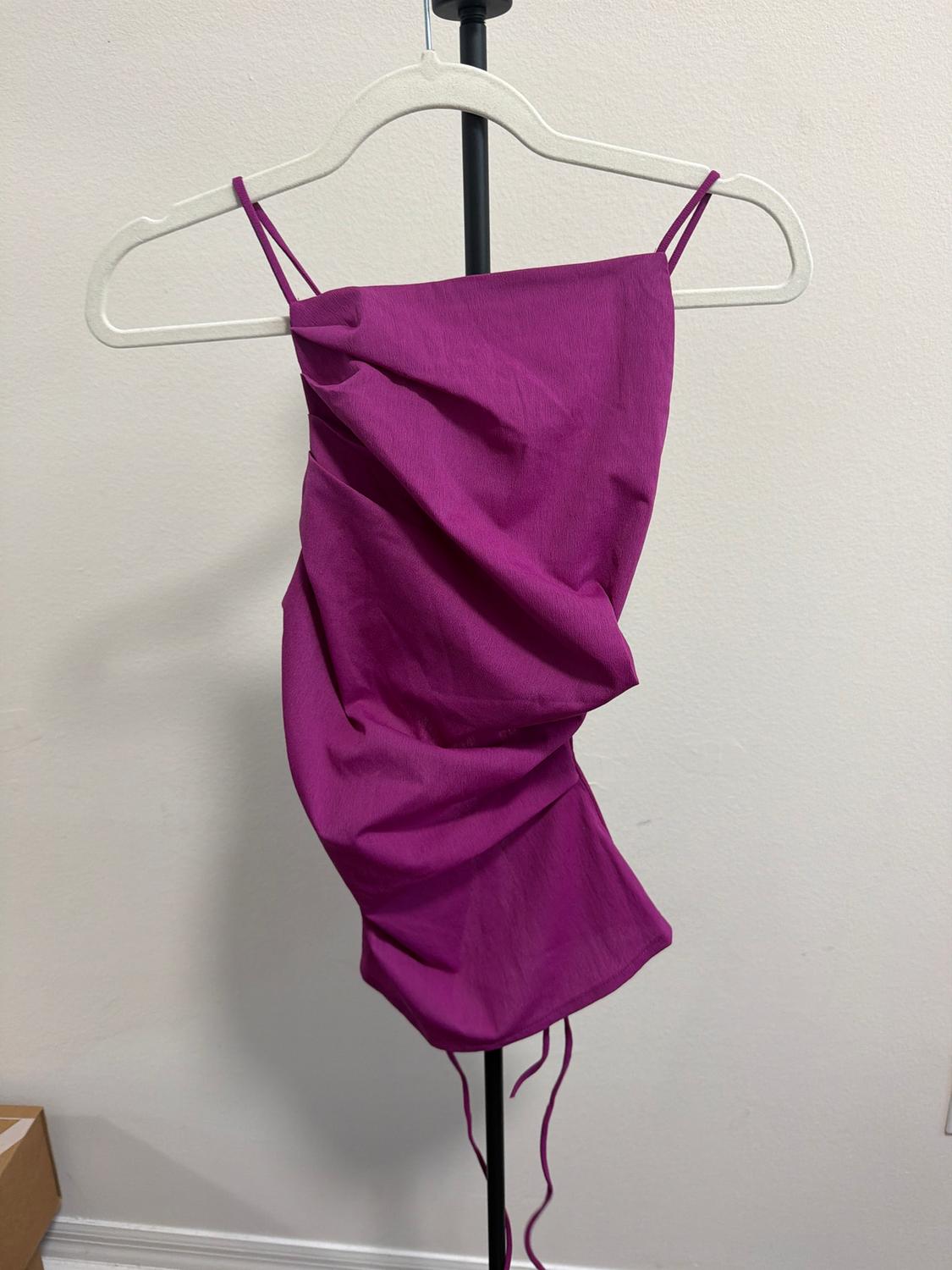 Fuchsia top with thin straps on a white hanger against a white background. Draped fabric with hanging drawstrings.