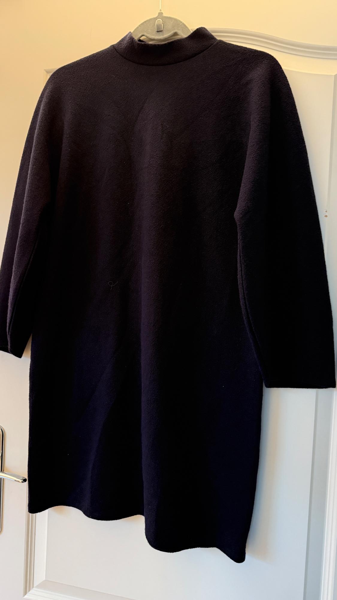 Black long-sleeved dress hanging on a hanger over a white door. The fabric looks soft and warm.