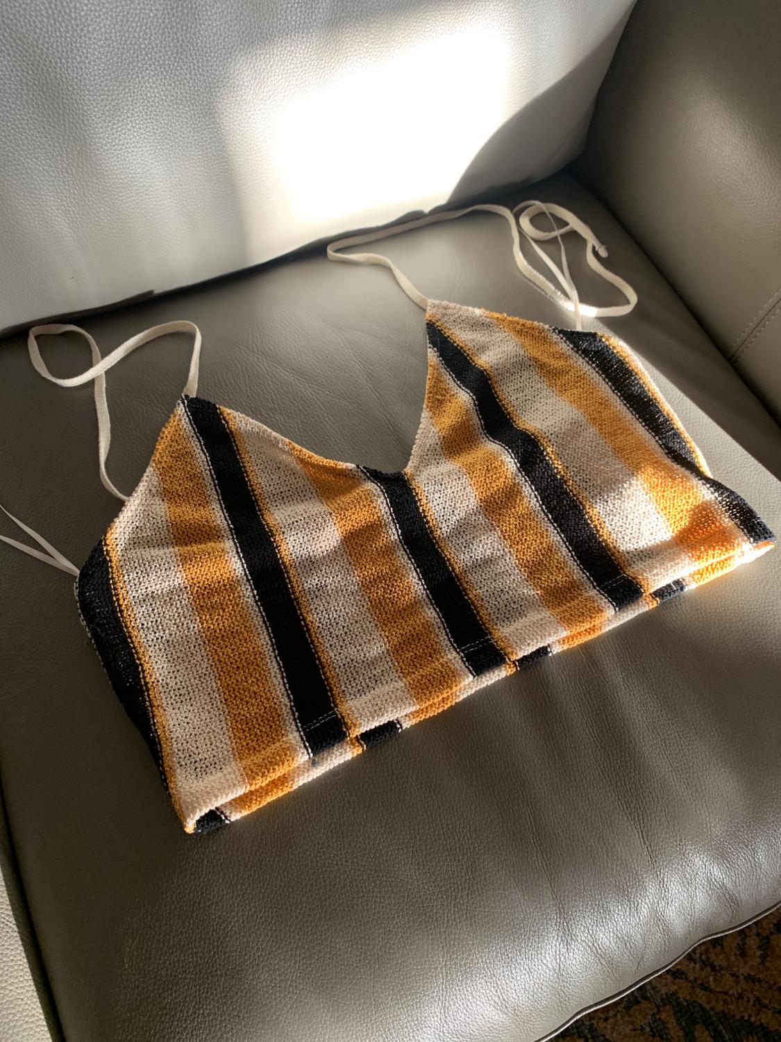 Strap top with horizontal black, white, and mustard stripes, on a grey sofa lit by sunlight.