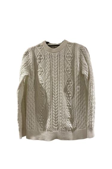 Front view of white sweater with cable knit design.