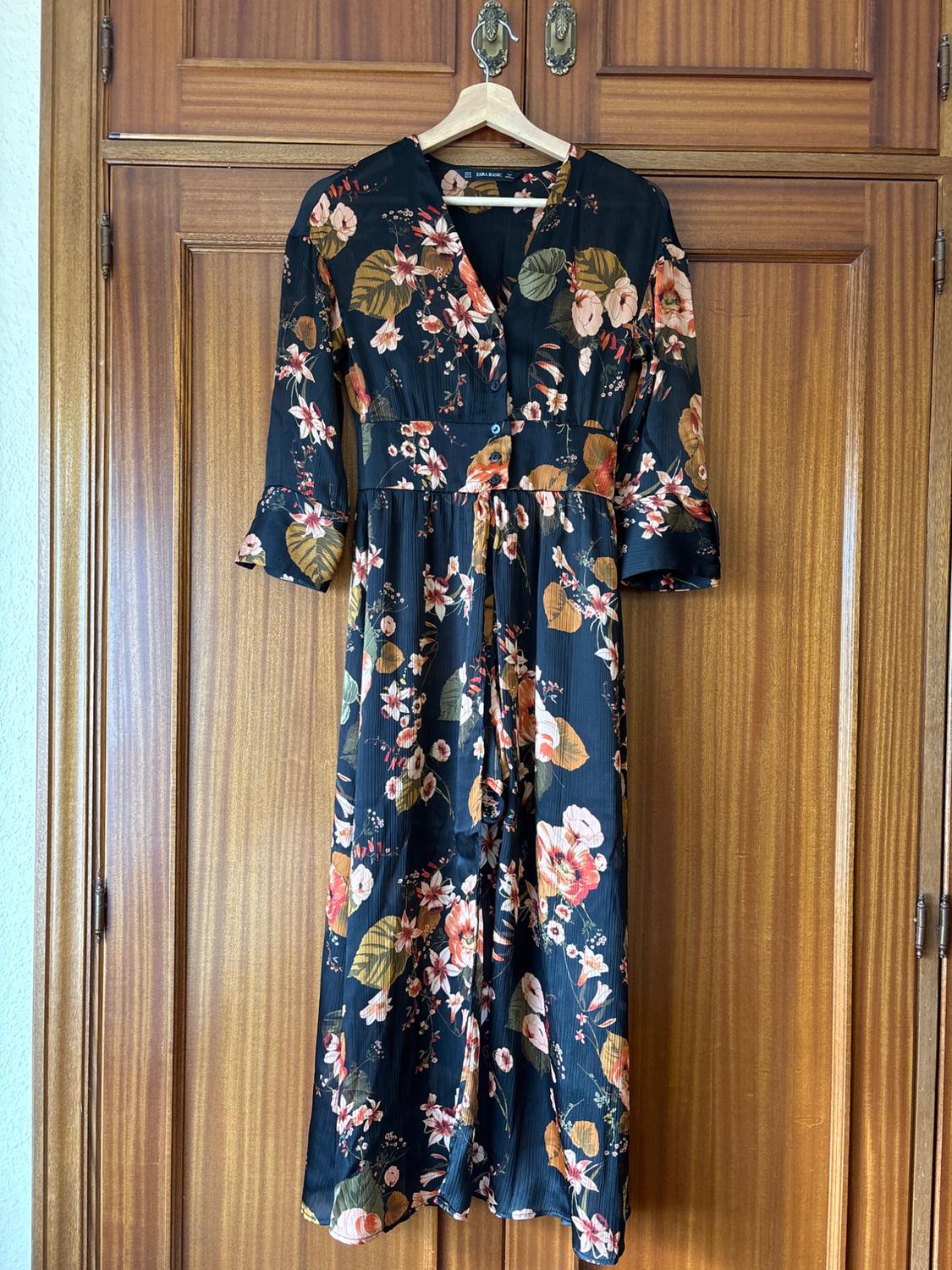 Floral maxi dress hanging on a wooden hanger in front of a wooden wardrobe door. Light brown background.
