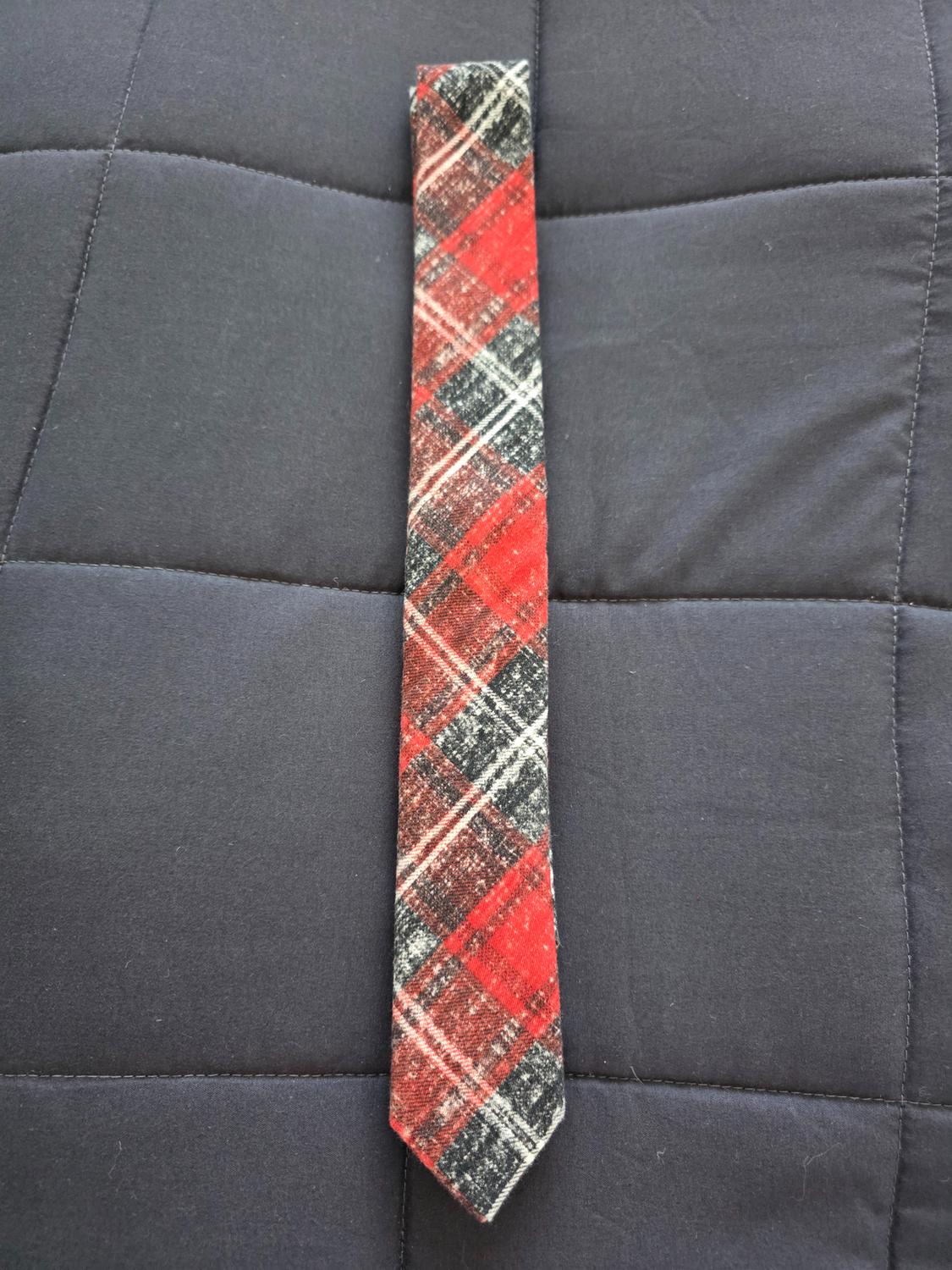 Red, black, and white checked tie on a dark grey padded surface.