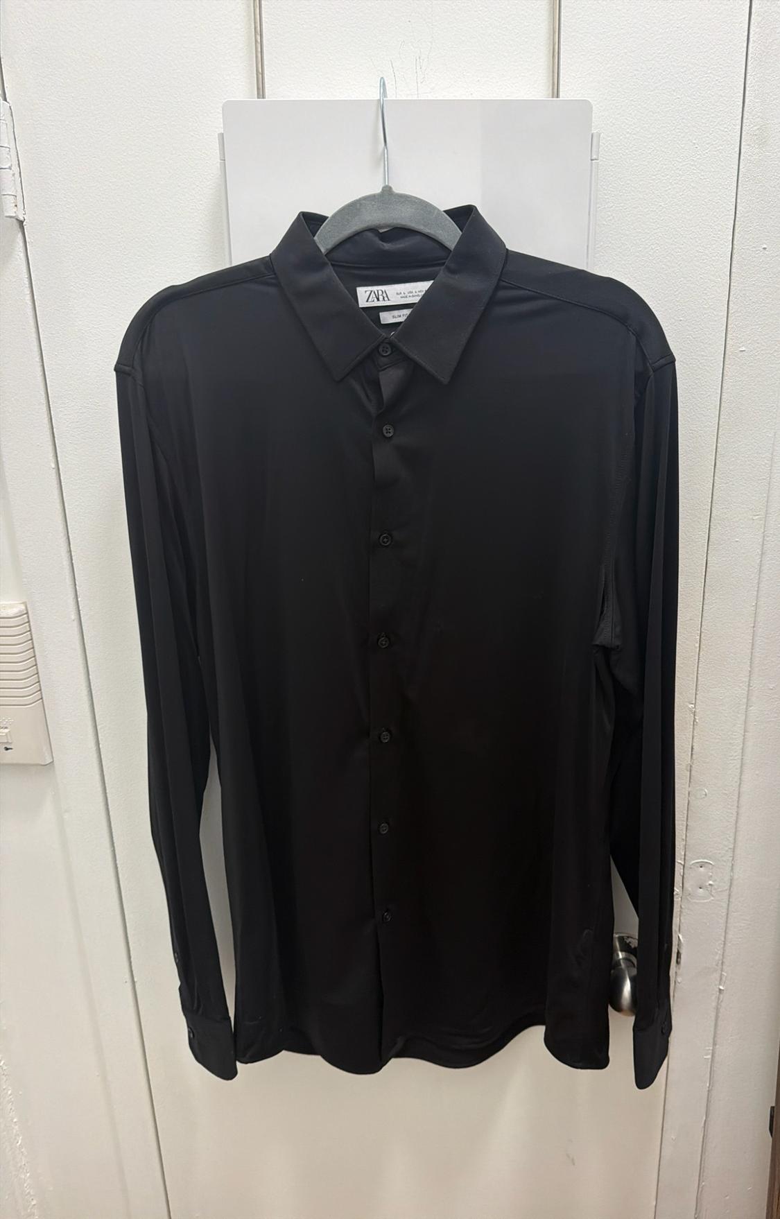 Black long-sleeved shirt hanging on a hanger over a white door. The label reads ZARA and SLIM FIT.
