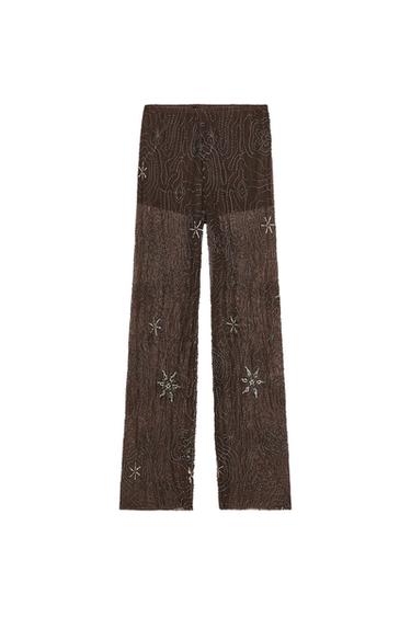 Front view of semi-sheer chocolate trousers with beads and sequins in a floral pattern. Inner shorts-style lining.