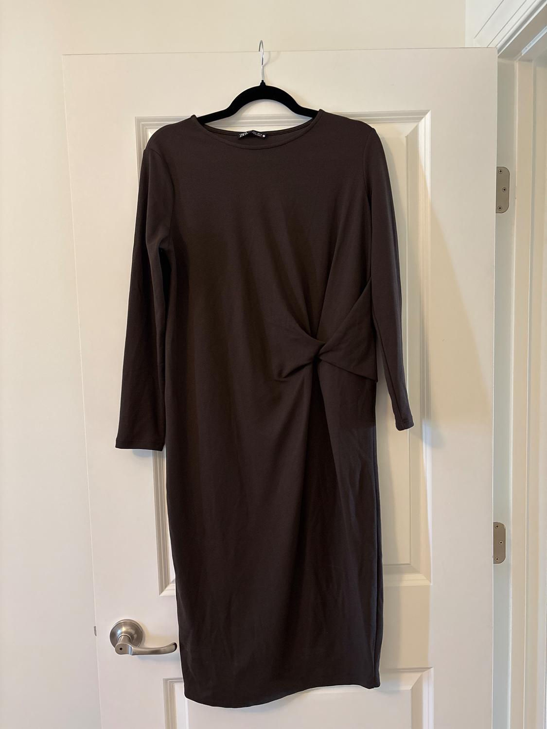 Brown, long-sleeved dress with knot detail at the waist, hanging on a hanger over a white door.