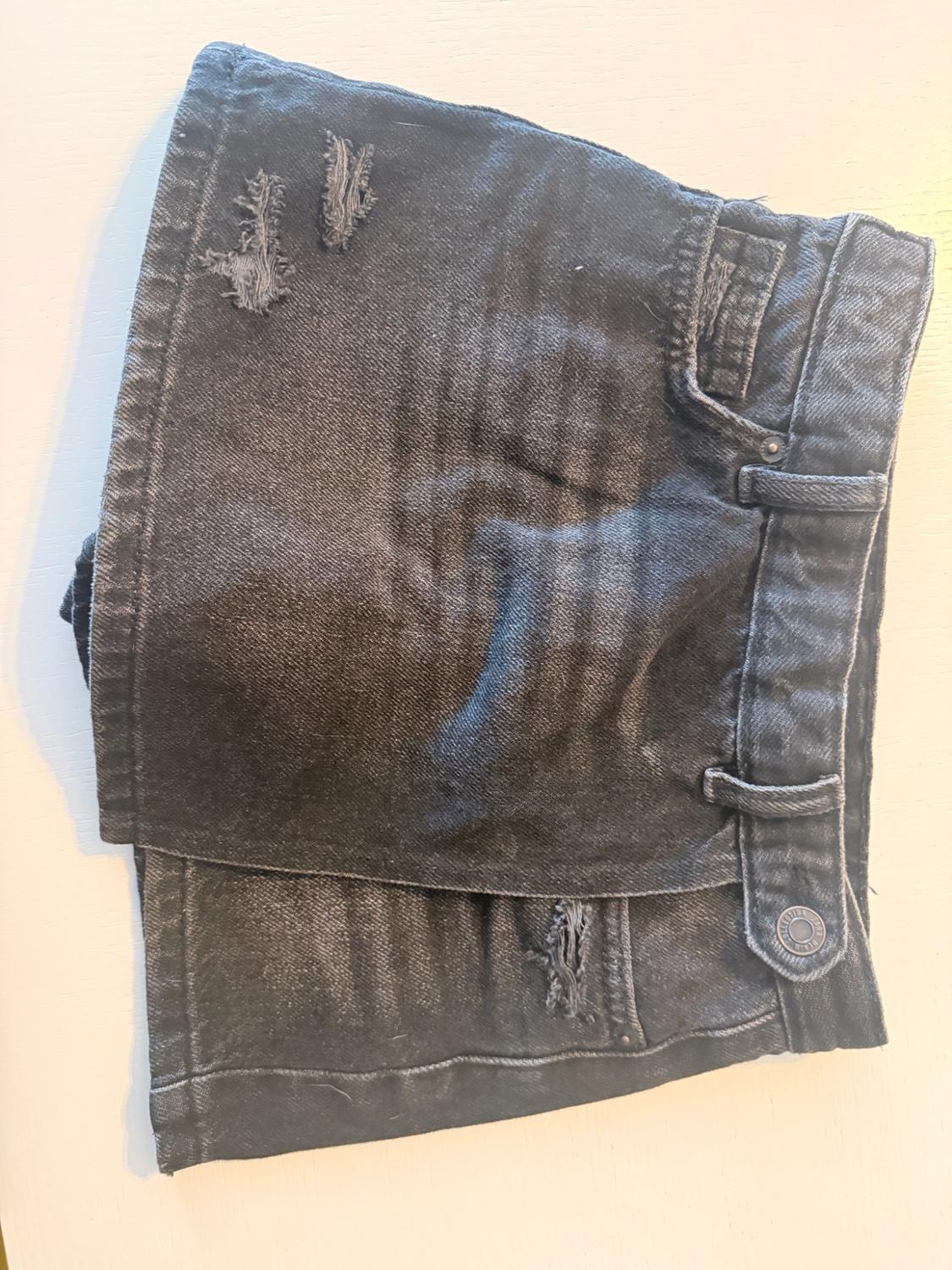 Black casual-style denim skirt with an asymmetrical panel and distressed detailing, laid flat on a white background.