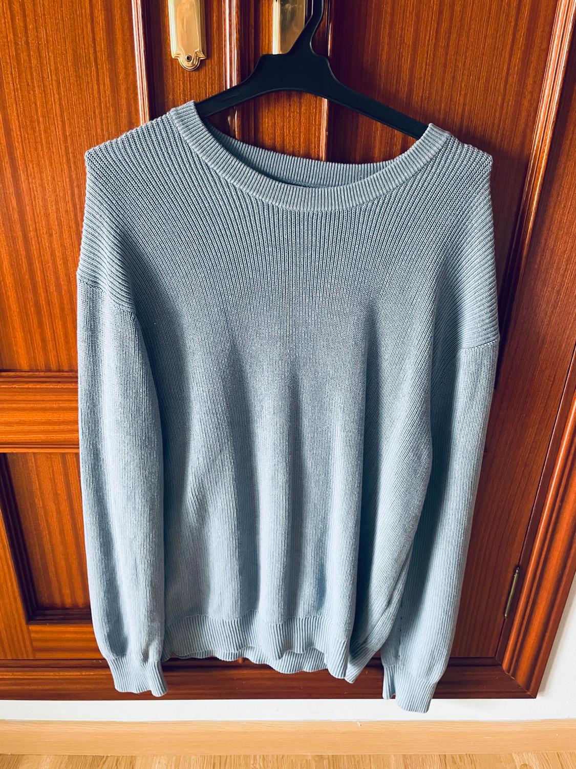 Grey knitted jumper hanging on a black hanger over a brown wooden door.